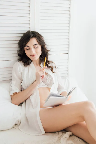 Flickan skriver i en anteckningsbok i sängen — Stockfoto