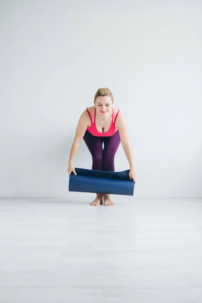 Donna in camera bianca diffonde un tappetino yoga — Foto Stock