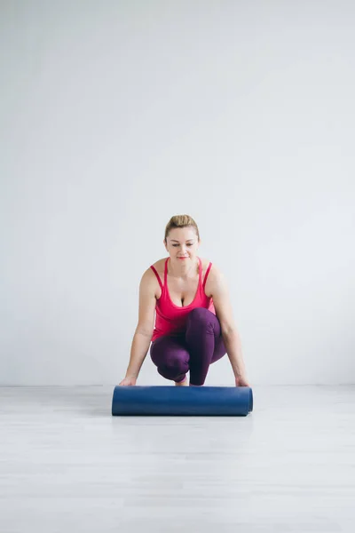 Donna in camera bianca diffonde un tappetino yoga — Foto Stock