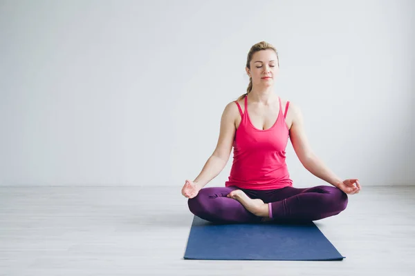 Mujer joven en una habitación blanca haciendo ejercicios de yoga  . — Foto de Stock