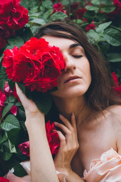 Chica de pie contra un fondo arbustos con rosas rojas — Foto de Stock
