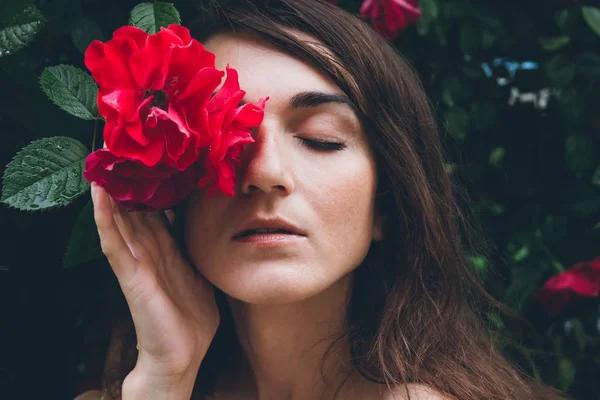 Mädchen steht vor einem Hintergrund Büsche mit roten Rosen — Stockfoto