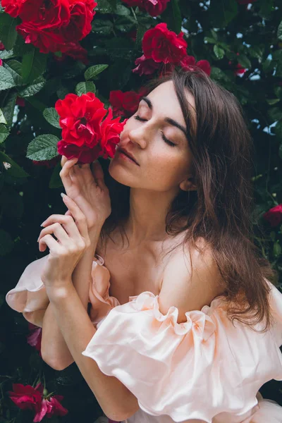 Chica de pie contra un fondo arbustos con rosas rojas — Foto de Stock