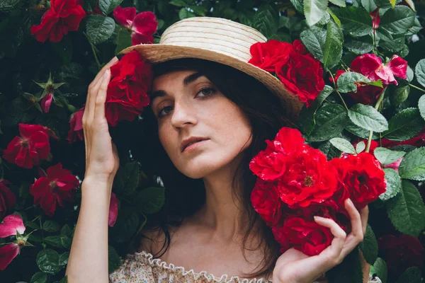 Mädchen steht vor einem Hintergrund Büsche mit roten Rosen — Stockfoto