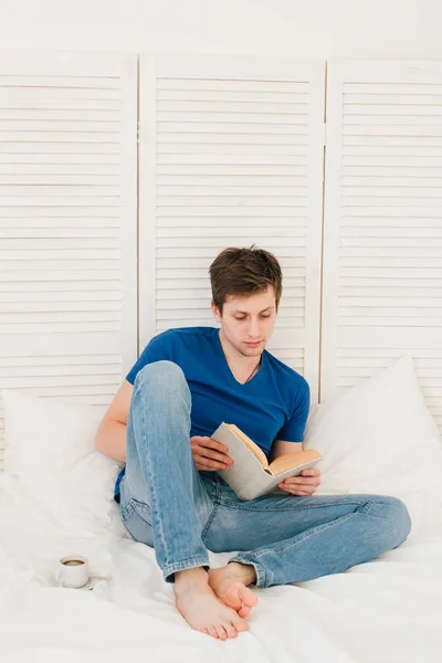 Человек, читающий книгу, сидя на кровати — стоковое фото