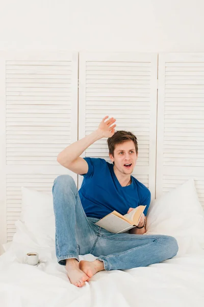 Hombre leyendo un libro sentado en la cama — Foto de Stock