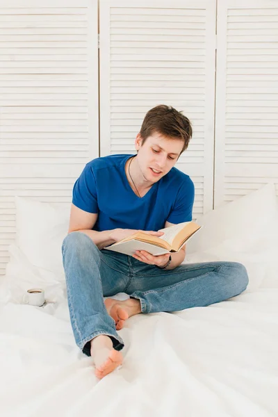 Человек, читающий книгу, сидя на кровати — стоковое фото