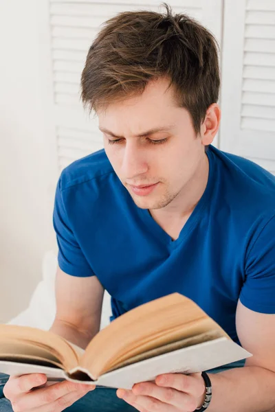 Yatakta oturmuş kitap okurken erkek — Stok fotoğraf