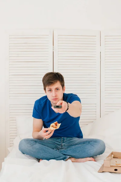 Hombre viendo la televisión sentado en la cama y comiendo pizza —  Fotos de Stock