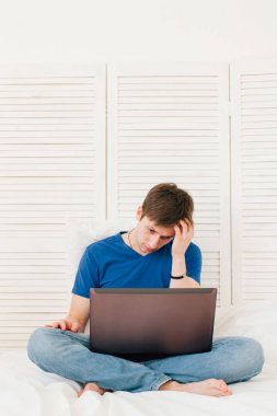 Yatakta oturmuş bir dizüstü çalışan adam 