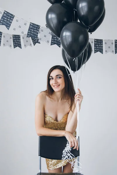 Mädchen im goldenen Kleid mit schwarzen Luftballons — Stockfoto