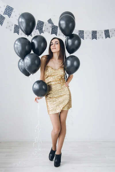 Menina em um vestido de ouro com balões pretos — Fotografia de Stock
