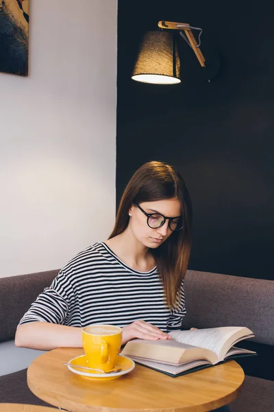 Девушка в очках читает книгу в кофейне — стоковое фото