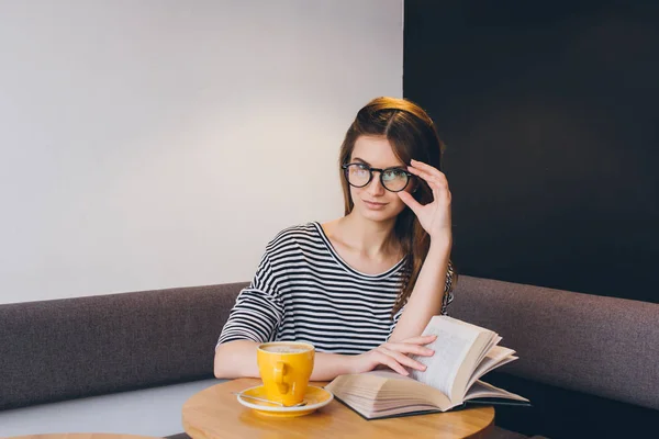 Девушка в очках читает книгу в кофейне — стоковое фото