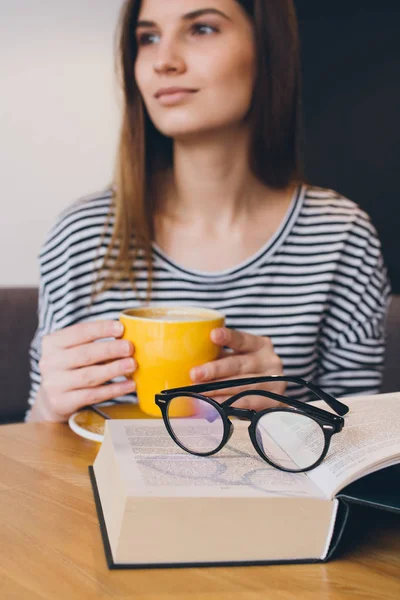 Девушка в очках читает книгу в кофейне — стоковое фото