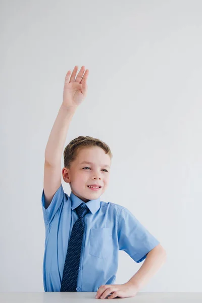 Školák ve školní uniformě zvedne ruku na stůl — Stock fotografie