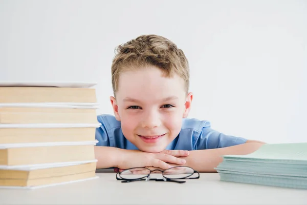 Colegial en uniforme escolar sentado en un escritorio con libros de texto y — Foto de Stock