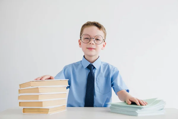 Estudante de uniforme escolar sentado em uma mesa com livros didáticos e — Fotografia de Stock