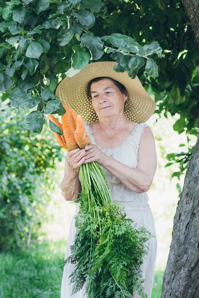 Portrait of an elderly woman in a hat holding a carrot — Stock Photo, Image