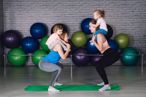 Two young sports mom and baby girls do exercises together in the