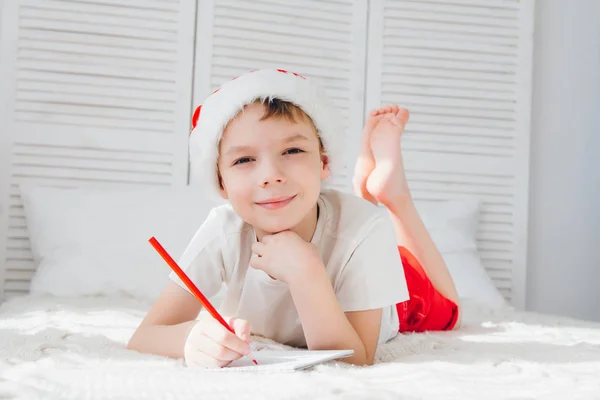 Rapaz de boné vermelho escreve uma carta ao Pai Natal — Fotografia de Stock