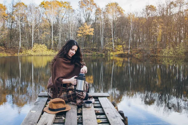 Girl drinking tea on a wooden bridge on a lake — Stock Photo, Image