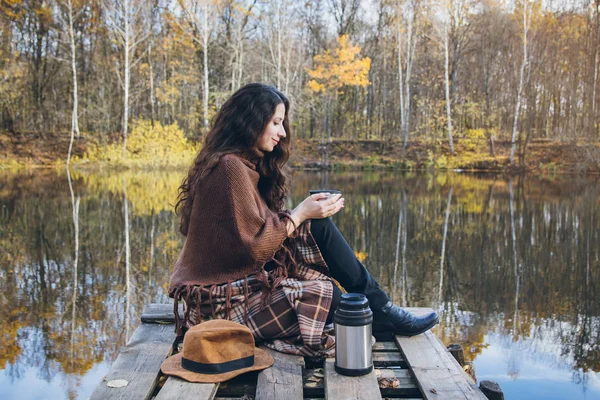 Girl drinking tea on a wooden bridge on a lake — Stock Photo, Image
