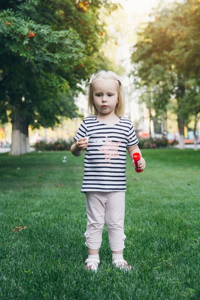 Маленькая девочка надувает мыльные пузыри на газоне — стоковое фото