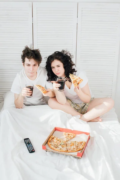 Пара смотрит телевизор в постели и ест пиццу — стоковое фото