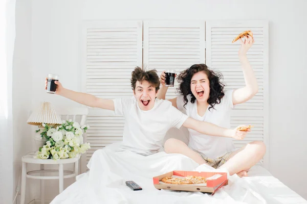 Coppia guardare la TV a letto e mangiare pizza — Foto Stock