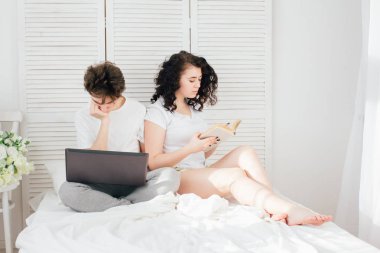 Adam çalışmalar için bir dizüstü bilgisayar, kız bir kitap okur.