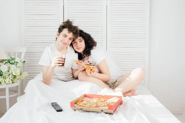Pareja viendo la televisión en la cama y comiendo pizza —  Fotos de Stock