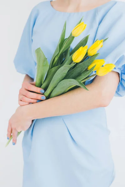 Chica en un vestido azul sostiene un ramo de tulipanes amarillos — Foto de Stock