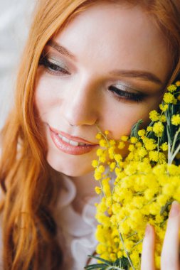 Uzun beyaz elbiseli bir Mimosa 'lı kızıl saçlı güzel bir kızın portresi. Bahar konseri. Tonlama.