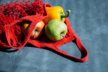 Kırmızı ağlı alışveriş torbası gri arka planda elma ve biberli alışveriş torbası. Çevre dostu yaşam tarzı kavramı. Tonlama. Seçici odak.