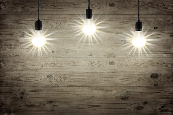Tres bombillas que brillan sobre el fondo de textura de madera marrón —  Fotos de Stock