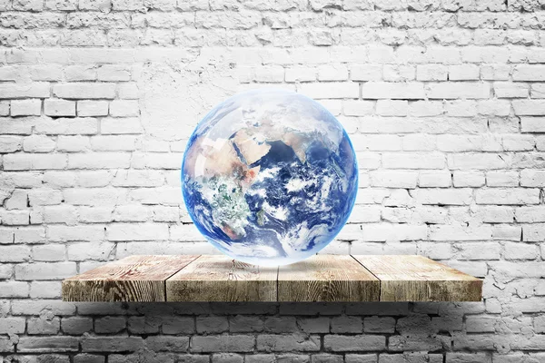 Earth globe on wood shelf over white brick background