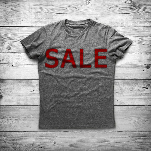 Grey shirt with inscription "sale" over wood background — Stock Photo, Image