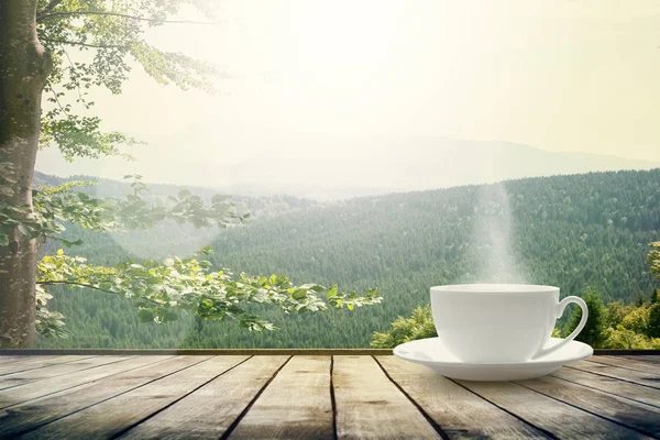 Cup with tea on table over mountains landscape with sunlight. — Stock Photo, Image