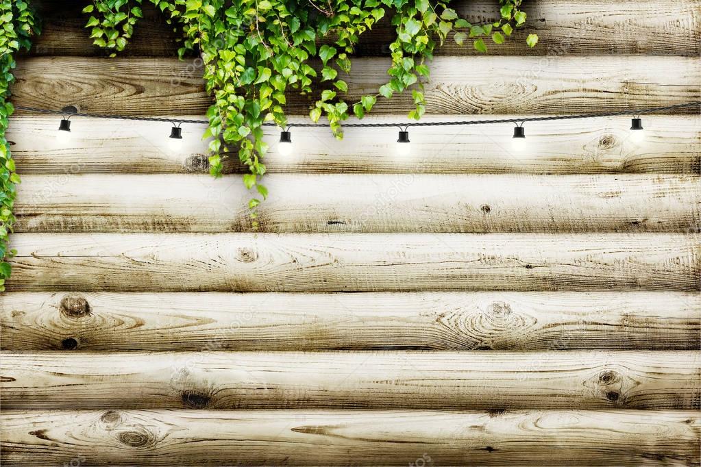 Garland lamps over wooden board fence with green leaves. Decoration background