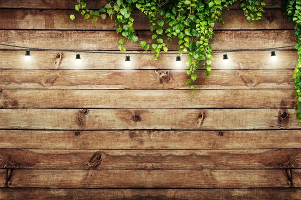 Lámparas de guirnalda sobre valla de madera con hojas verdes. Fondo decorativo —  Fotos de Stock