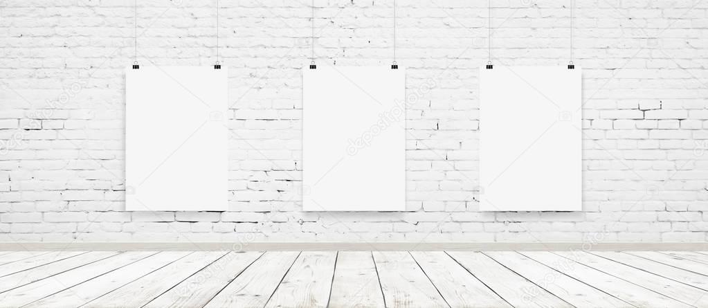 Tree white blank posters with binders in interior with white brick wall and wooden floor