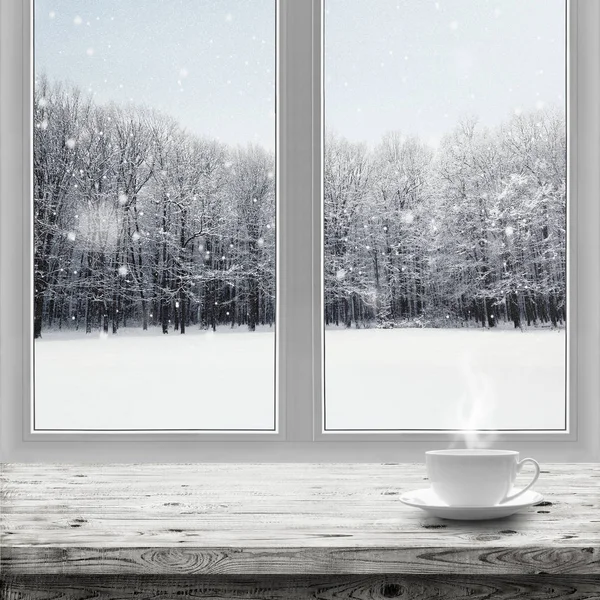 Bevanda calda in tazza sul tavolo sopra lo sfondo della foresta invernale attraverso la finestra — Foto Stock