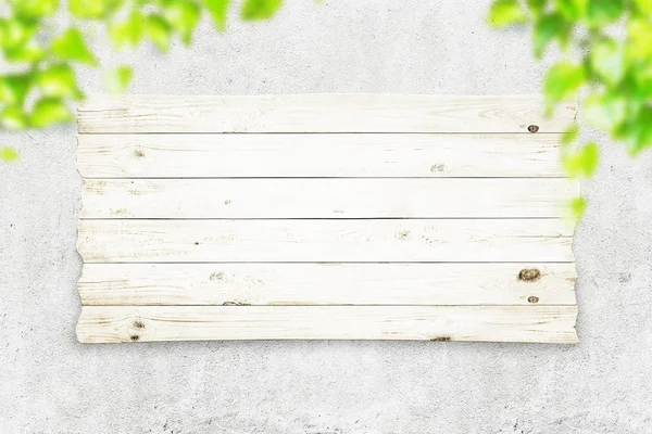 Tavola di legno su muro di cemento e foglie verdi. Sfondo primavera — Foto Stock