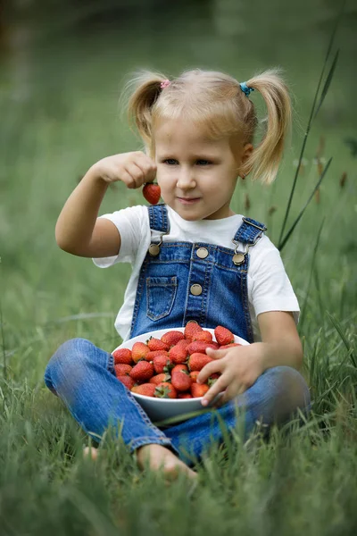 Mała dziewczynka z jaskrawoczerwone jagody w białe płytki na trawie w lecie — Zdjęcie stockowe