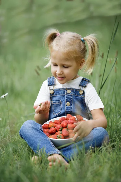 Een klein meisje met heldere rode bessen in de witte plaat op de — Stockfoto
