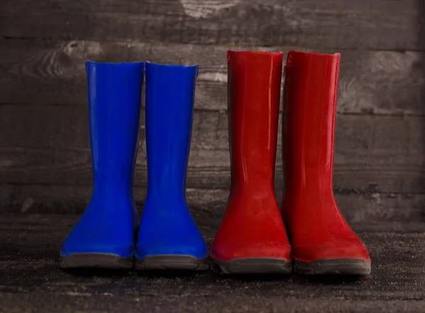 Botas de goma azules rojas para niños sobre un fondo de madera . — Foto de Stock