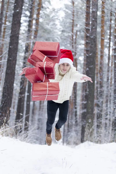 Подросток в шляпе Санта-Клаус собирает подарки в снежном лесу в снегу , — стоковое фото