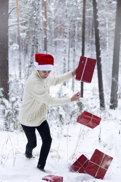 Подросток в шляпе Санта-Клаус собирает подарки в снежном лесу в снегу , — стоковое фото