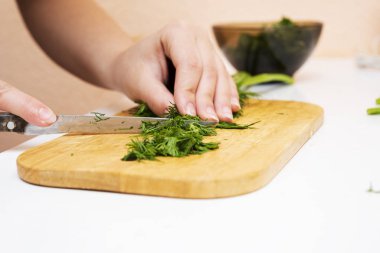 Eller kesme tahtasındaki bıçakla yeşillikleri kesiyor.